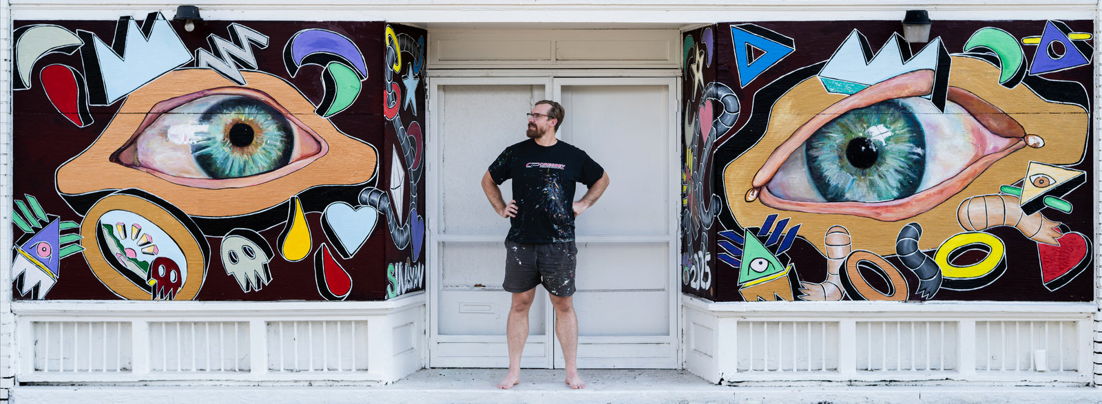 Richard Sullivan standing between his eye murals at BNK St. Gallery + Studio